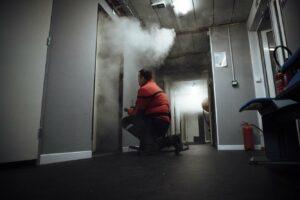 Un homme de la sécurité incendie se positionne devant une pièce d'où sort de la fumée