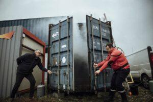 Deux hommes ouvrent un container, laissant sortir de la fumée de celui-ci